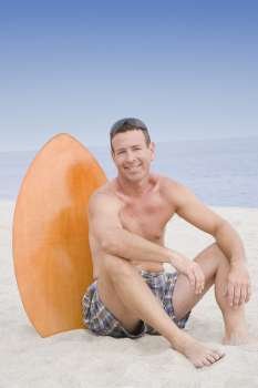 Portrait of a mature man sitting with a surfboard on the beach and smiling