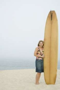 Portrait of a mature woman standing with a surfboard on the beach