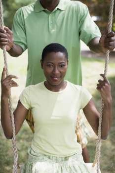 Portrait of a mid adult woman sitting on a rope swing with a mature man pushing her
