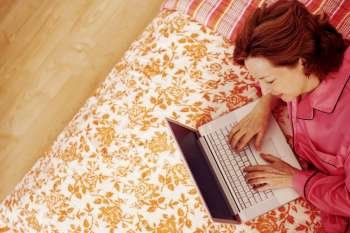 High angle view of a mature woman lying in bed using a laptop