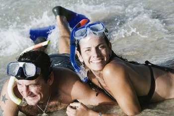 Mid adult couple wearing snorkeling gear and lying on the beach