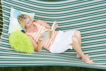 High angle view of a mid adult woman lying in a hammock and reading a book