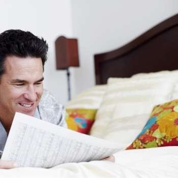 Mature man lying on the bed reading a newspaper