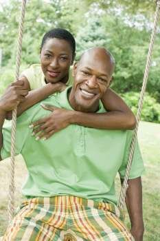 Portrait of a mature man sitting on a rope swing with a mid adult woman embracing him