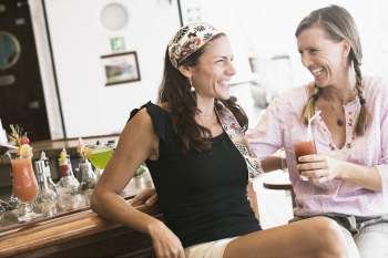Two mid adult women sitting at a bar counter and smiling