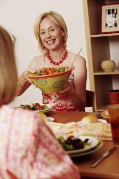 Mature woman giving a bowl of salad to her friend and smiling