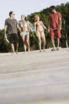 Two mid adult couples holding hands and walking on a jetty