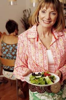 Portrait of a mature woman holding a plate of salad and her friend sitting behind her
