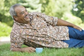 Senior man reclining in a lawn and holding a tea cup