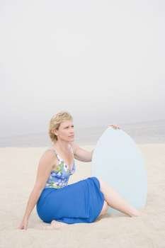 Mature woman sitting on the beach and holding a body board