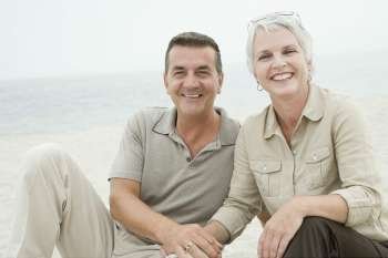 Portrait of a mature couple sitting on the beach and smiling