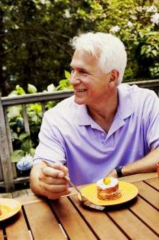 Mature man sitting with a plate of dessert in front of him and smiling