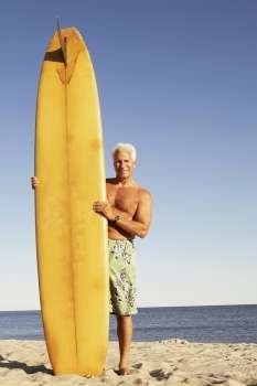Portrait of a mature man standing on the beach holding a surfboard