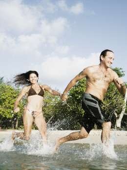 Mid adult couple running in water on the beach