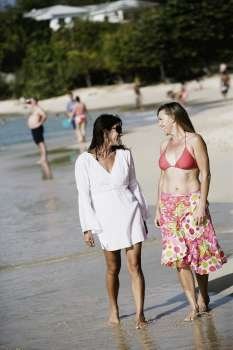 Two mid adult women walking on the beach with tourists in the background