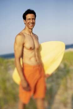 Portrait of a mature man standing on the beach and holding a wooden surfboard