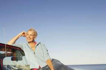 Mature woman sitting on the bonnet of a sports utility vehicle and looking away