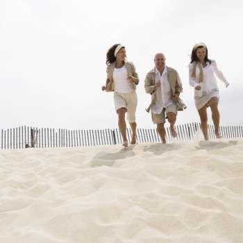 Two mature women and a mature man running on the beach