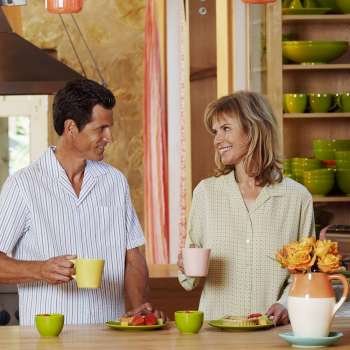 Mature couple holding cups in the kitchen and smiling