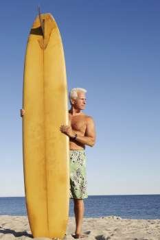 Mature man standing on the beach holding a surfboard