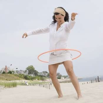 Mature woman playing with a plastic hoop and smiling on the beach