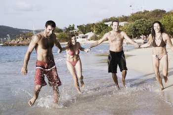 Two mid adult couples holding hands and running on the beach