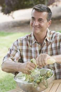 Mature man husking a corn over a bowl