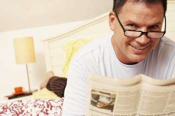 Portrait of a mature man lying in bed and holding a newspaper