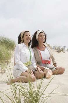 Two mature women kneeling on the beach and smiling