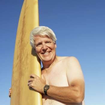 Portrait of a mature man holding a surfboard and smiling