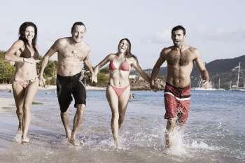 Two mid adult couples holding hands and running on the beach