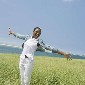 Mid adult woman standing on the beach with her arms outstretched and laughing