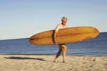 Portrait of a mature man holding a surfboard and walking on the beach