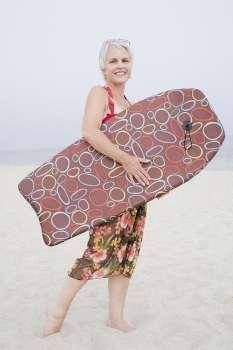 Side profile of a mature woman holding a body board on the beach