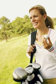 Close-up of a mid adult woman holding a golf ball and a golf bag