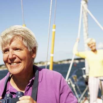 Mature man holding a pair of binoculars in a boat with a mature woman standing behind him