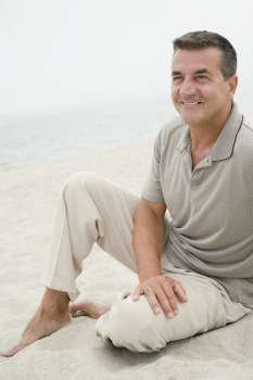 Mature man sitting on the beach and smiling
