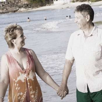 Mature woman holding a senior man´s hand and walking on the beach