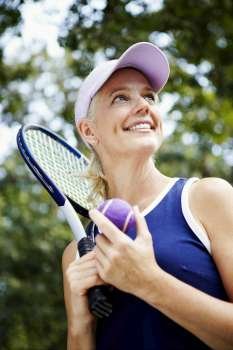 Low angle view of a mature woman holding a tennis racket and a tennis ball
