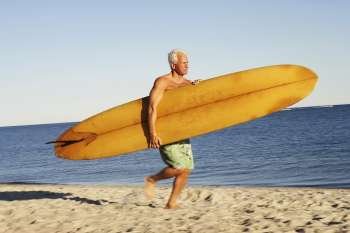 Side profile of a mature man holding a surfboard and walking on the beach