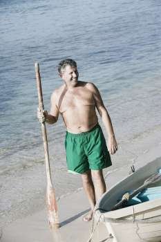 High angle view of a senior man holding an oar on the beach