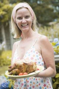 Portrait of a mid adult woman holding a plate of roast chicken and smiling