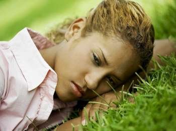 Close-up of a young woman lying on the grass and looking serious