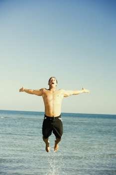 Mid adult man jumping on the beach with his arms outstretched 
