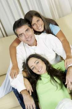 Portrait of a mature man and his two daughters sitting on a couch and smiling