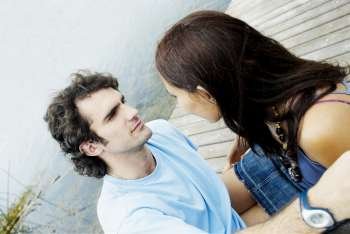 Close-up of a young couple sitting at a pier and looking at each other