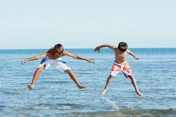 Teenage boy jumping with his brother in water with their arms outstretched