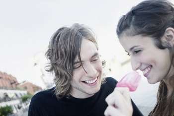 Close-up of a young woman eating an ice-cream with a teenage boy smiling
