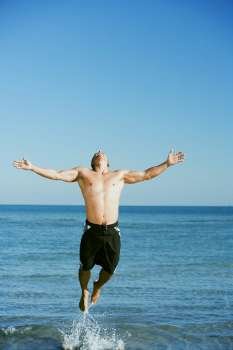 Mid adult man jumping on the beach with his arms outstretched