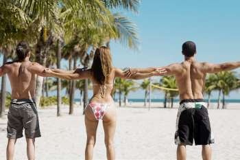 Rear view of a woman and two men standing with their arms outstretched on the beach